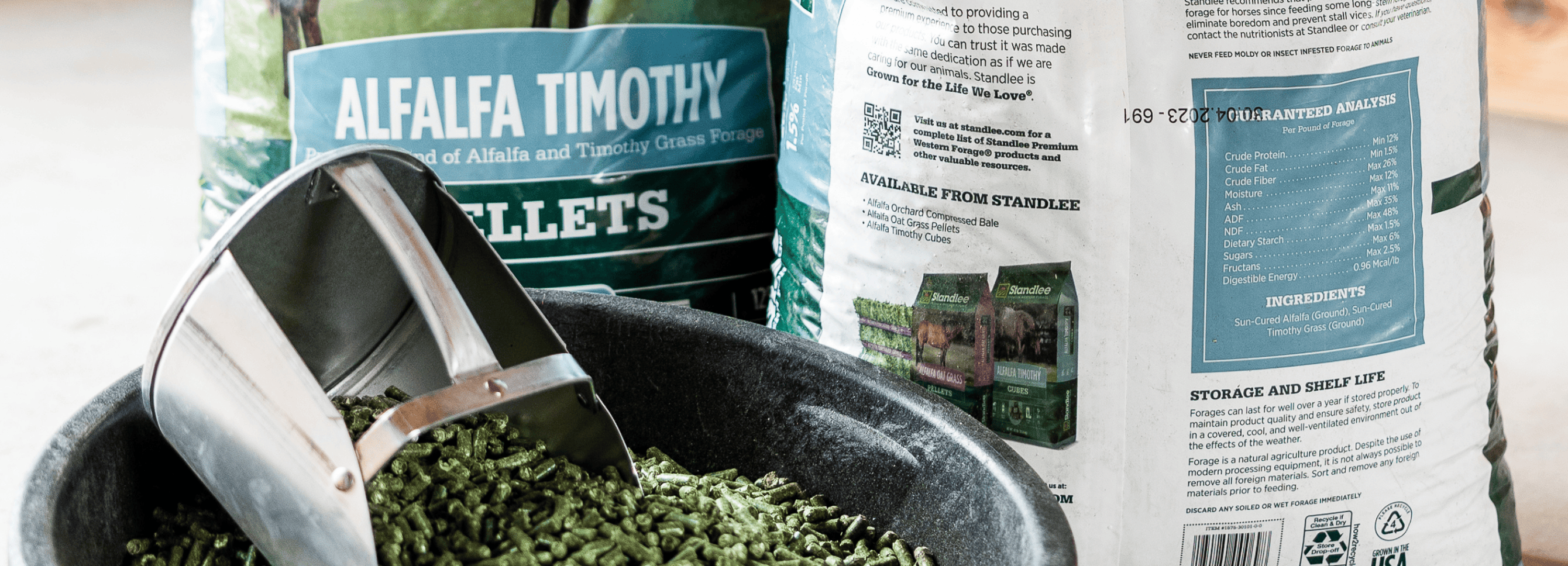 Close-up of Standlee Alfalfa Timothy Pellets being scooped from a feed tub with product bags displayed in the background.