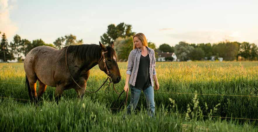 Woman walking horse in field.