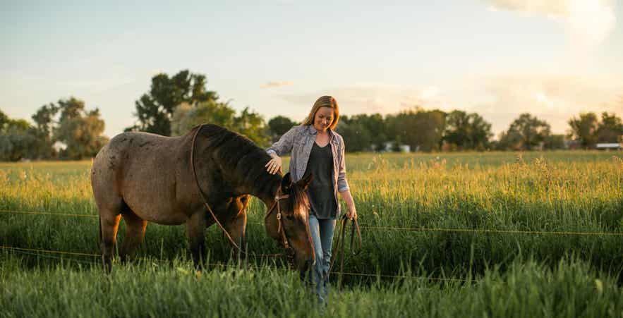 Women walking horse in green pasture.