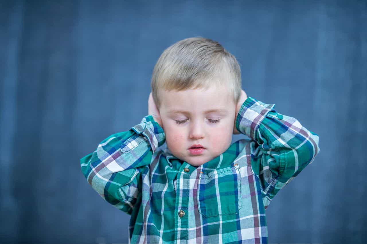 Kid with closed eyes covering ears with hands